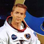 Portrait of Stuart A. Roosa wearing his Apollo 14 space suit and posing in front of the Apollo 14 mission logo