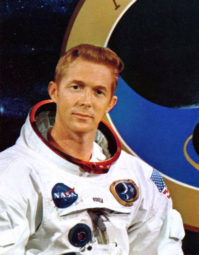 Portrait of Stuart A. Roosa wearing his Apollo 14 space suit and posing in front of the Apollo 14 mission logo