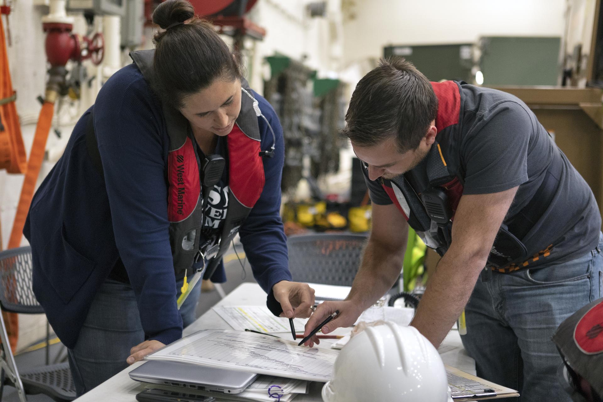 NASA Landing and Recovery Director Melissa Jones looks at a sheet of paper on a desk with a recovery team member.