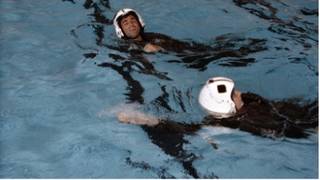 Astronauts wearing helmets and flight suits in the pool at Eglin Air Force Base in Pensacola, Florida, during water survival exercises. n