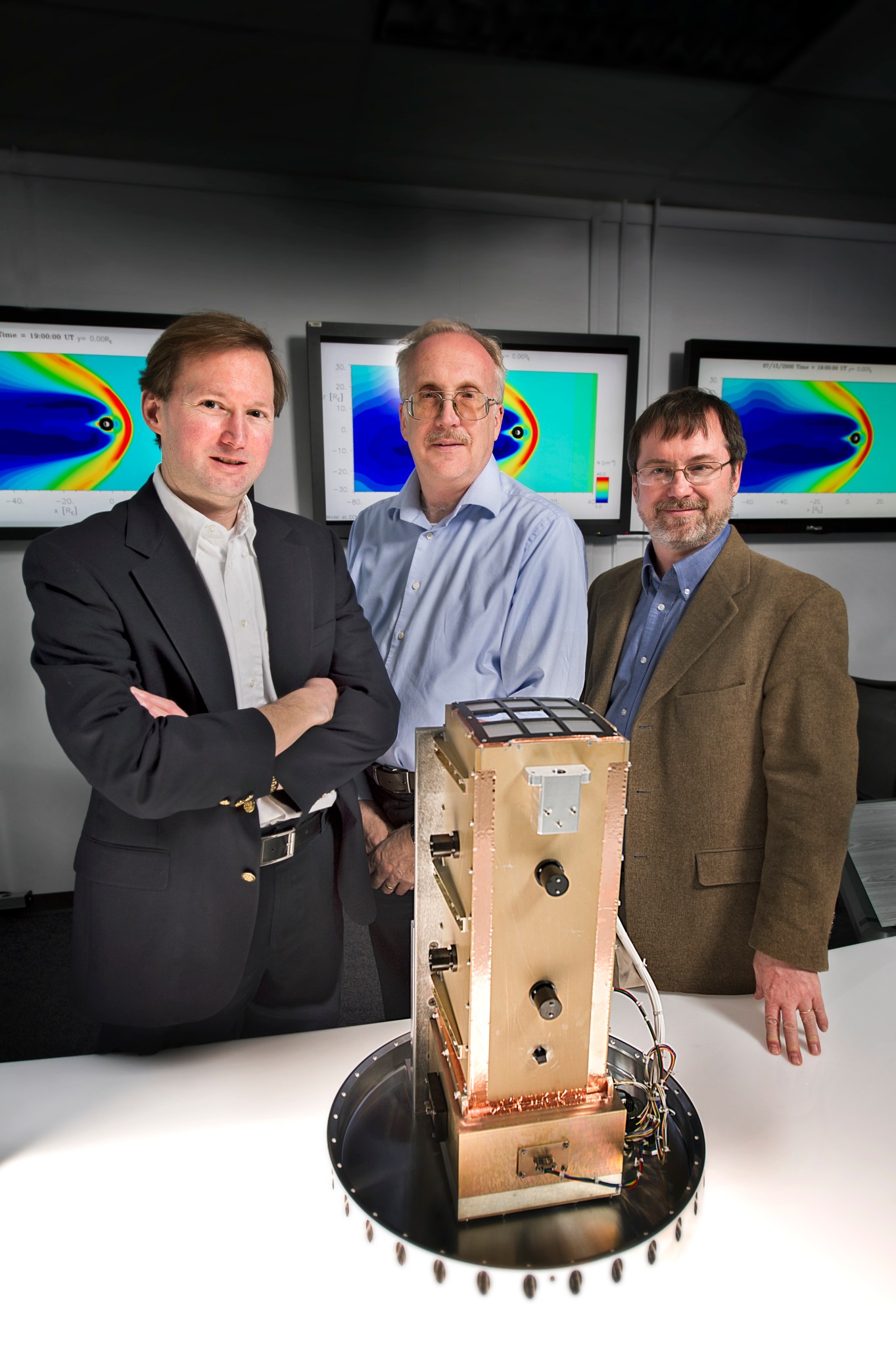 Three people stand behind a piece of space hardware