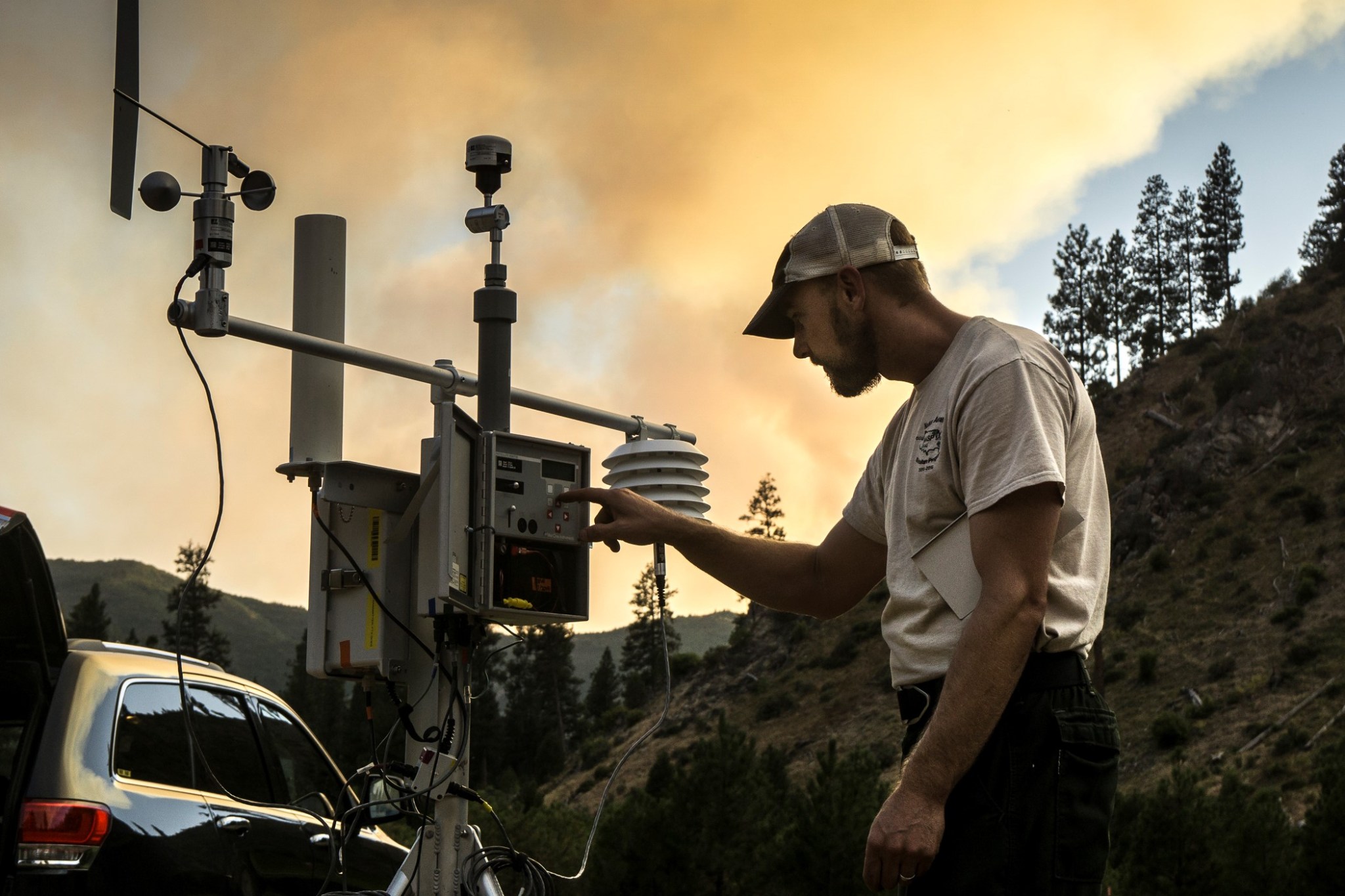 Photo of person at scientific instrument with smoke from a fire is in the background