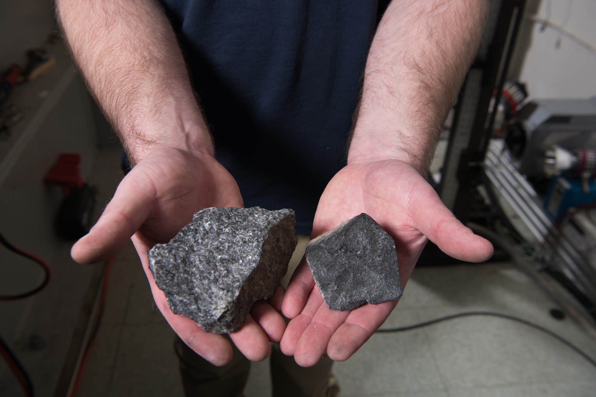 A close-up of an engineer holding two coarse-textured grey basalt rocks in his hands.