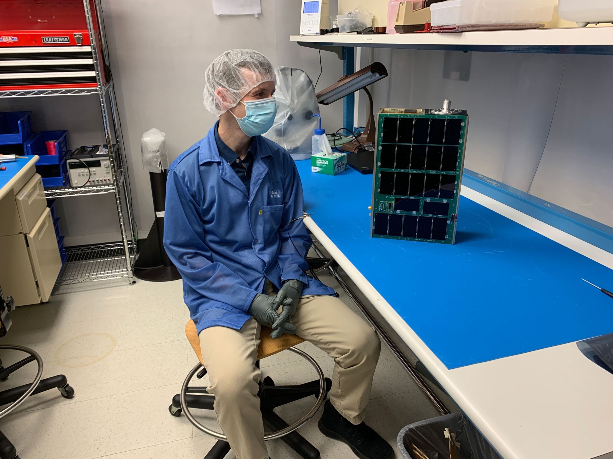 Scientist sitting in lab looking at cubesat.