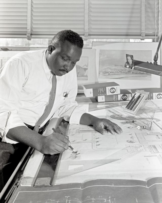 1961 black and white photo of Jessie Strickland at a drawing table, pencil in hand working on an engineering drawing.