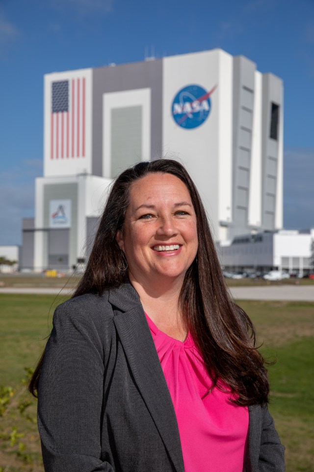 A photo of Kennedy Space Center's Elizabeth Kline with the Vehicle Assembly Building in the background.