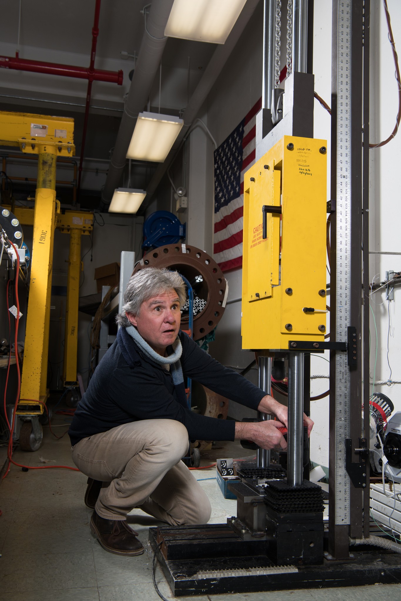 An engineer kneels before a tall yellow and silver crane device and adjusts its settings.