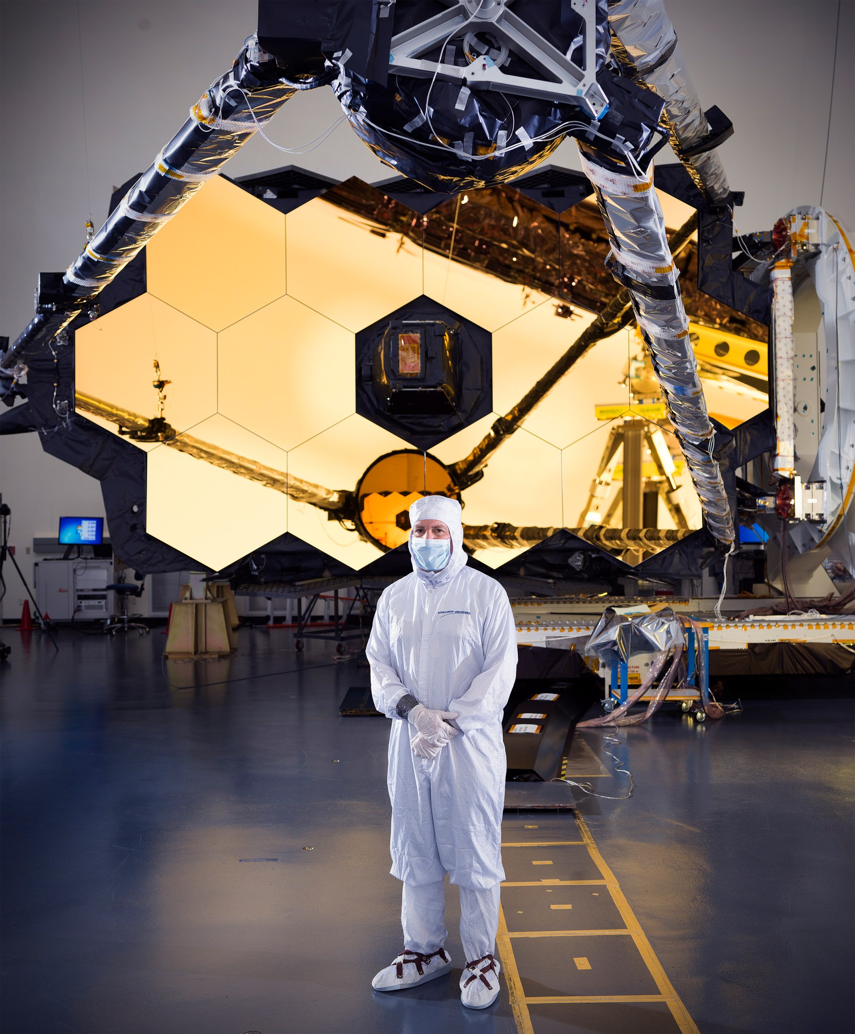 Feinberg, wearing a white "bunny suit" covering in the clean room, standing in from of the James Webb Space Telescope.