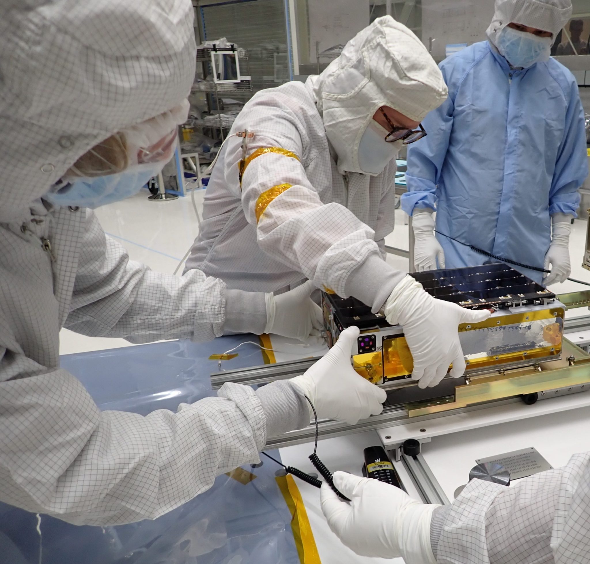 Technicians in clean suits working on CubeSat.