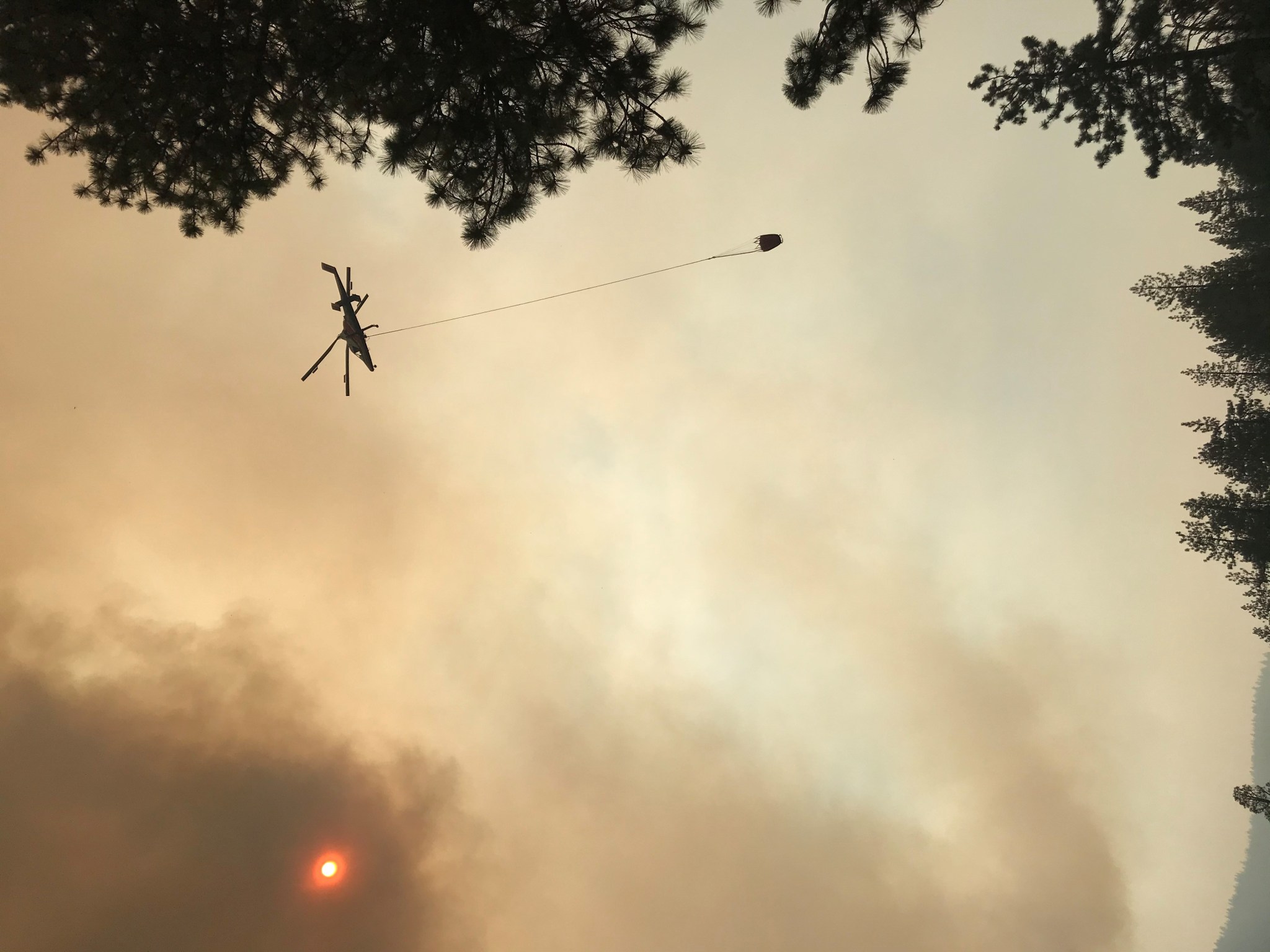A helicopter carrying a bucket in a smoky sky