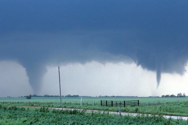 A photo of two tornadoes Kohler took while storm chasing. The land is green and flat, there's a fence in the middle of the land, in the sky, reaching down to the horizon are two tornados, on the left and right sides. 