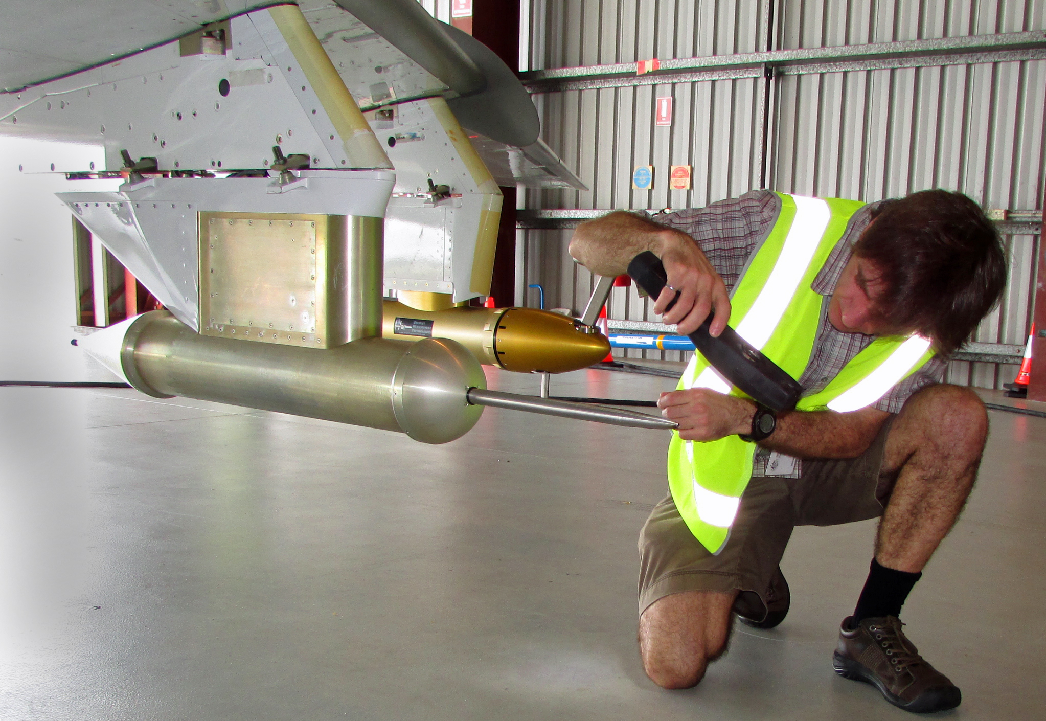 A researcher kneeling down inspecting the probe under the aircraft wing.