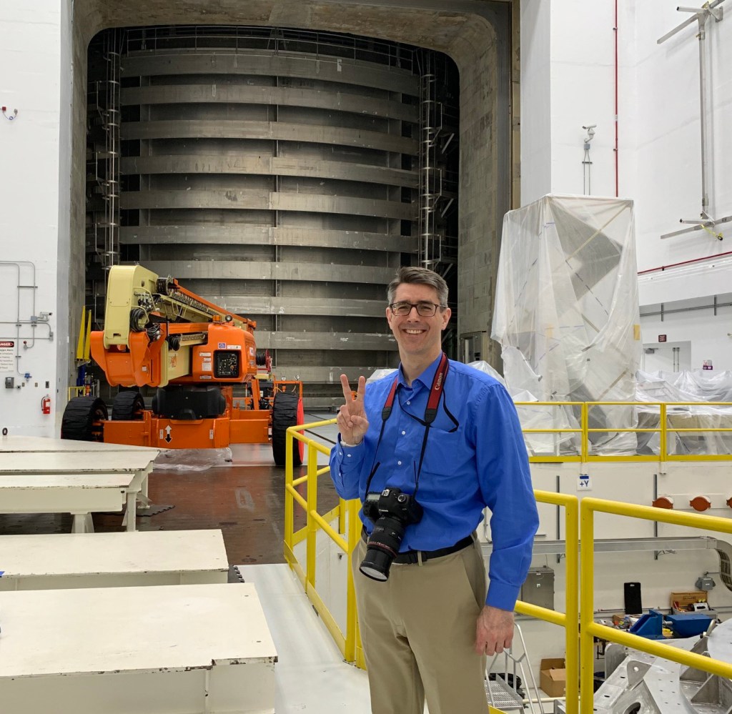 Man facing camera and giving the peace sign outside a NASA vacuum chamber.