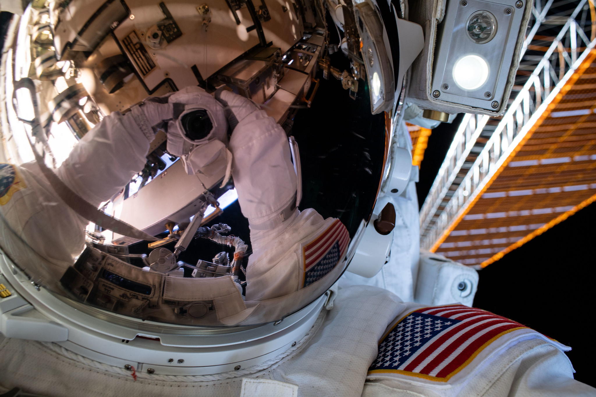 A spacewalker's spacesuit gloves and camera are reflected in the helmet visor during a six-hour and seven-minute spacewalk.