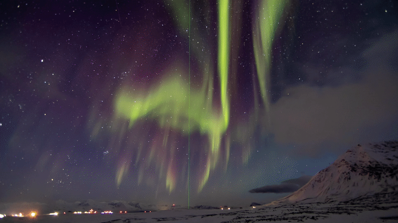 In this time-lapse movie, green and purple lights ripple and shift in the night sky over snow-covered ground. A green, vertical beam of light extends upward from the ground in the center of the view. 