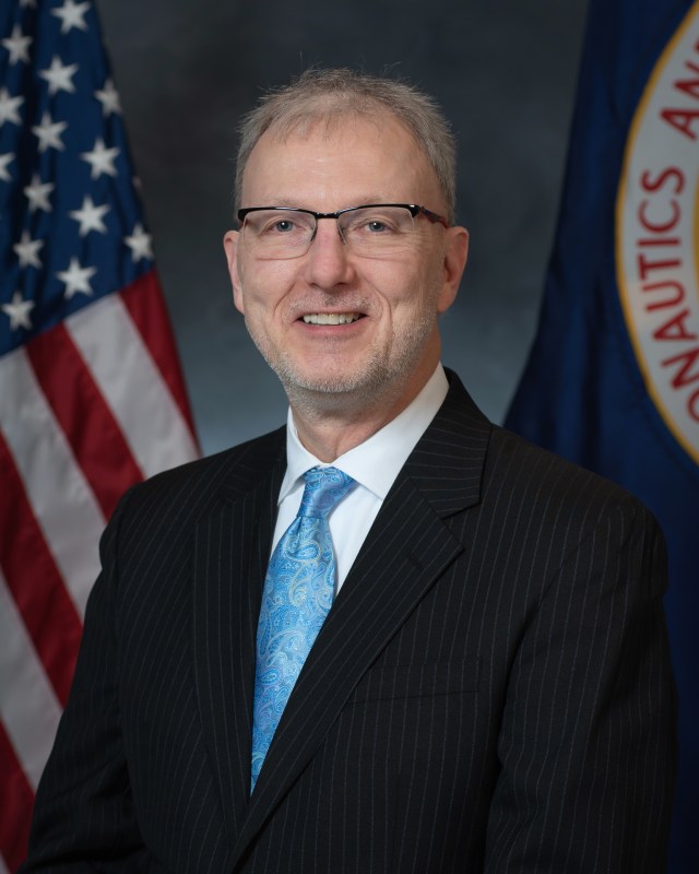 Michael Barrett portrait with U.S. and NASA flags in background