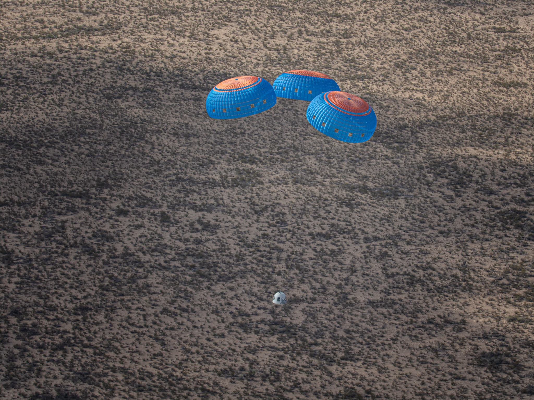 Capsule descending to Earth, attached to parachutes.