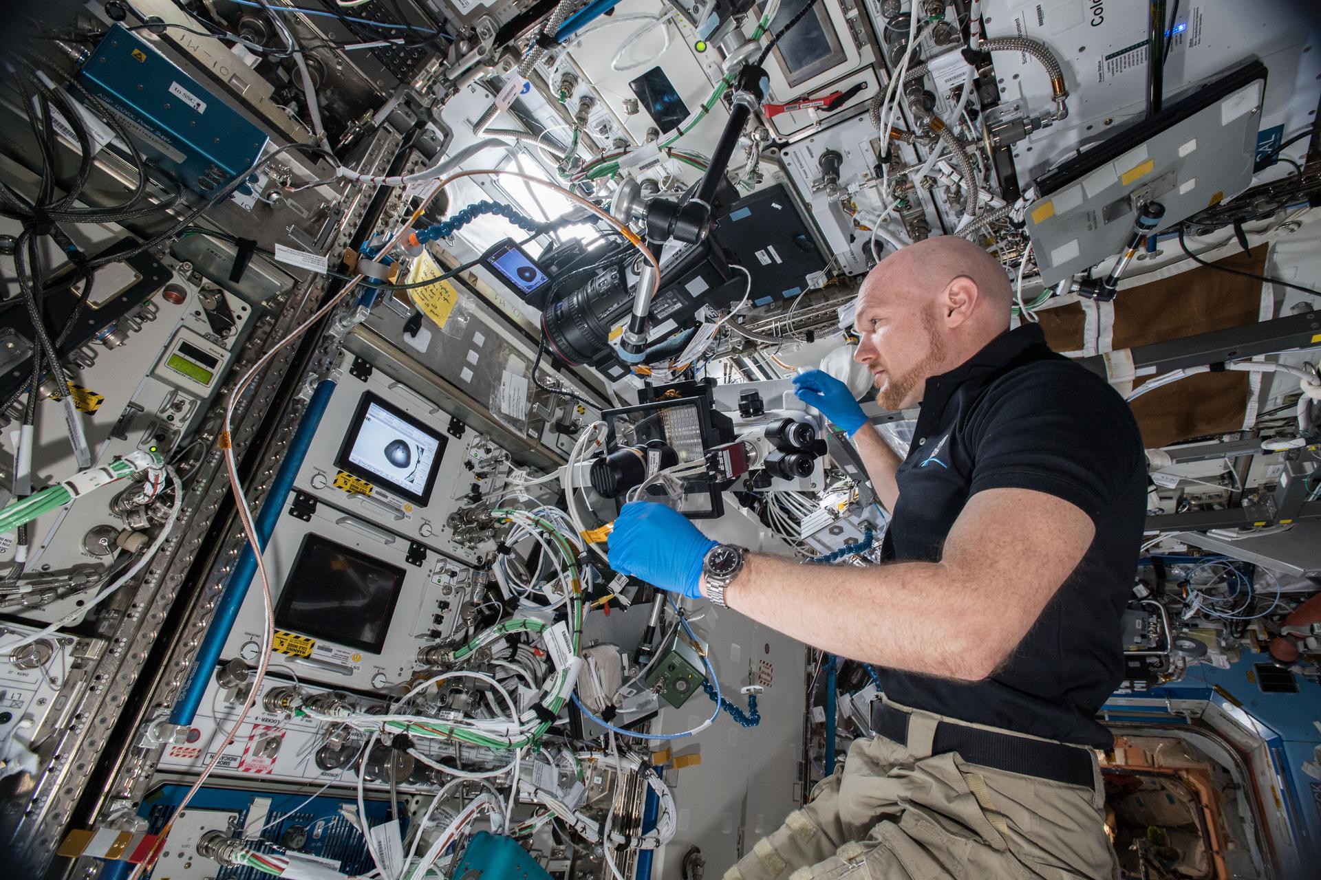 ESA (European Space Agency) astronaut Alex Gerst uses a microscope with the Space Automated Bioproduct Laboratory (SABL) Camera attached to document a Protein Crystal Growth (PCG) MicroG Card. T