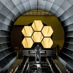A man in a white suit stands in front of the James Webb Space Telescope mirrors