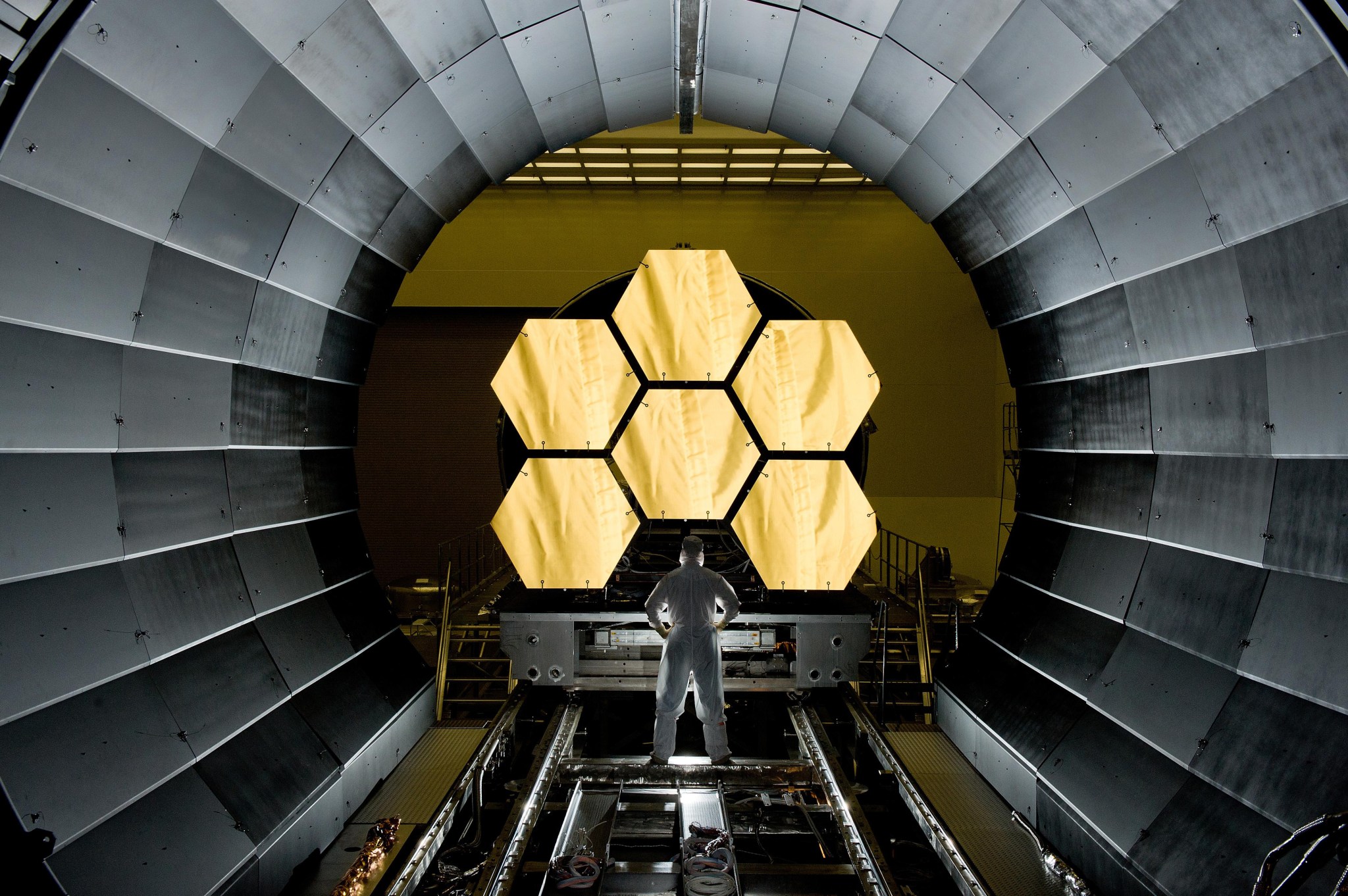 A man in a white suit stands in front of the James Webb Space Telescope mirrors