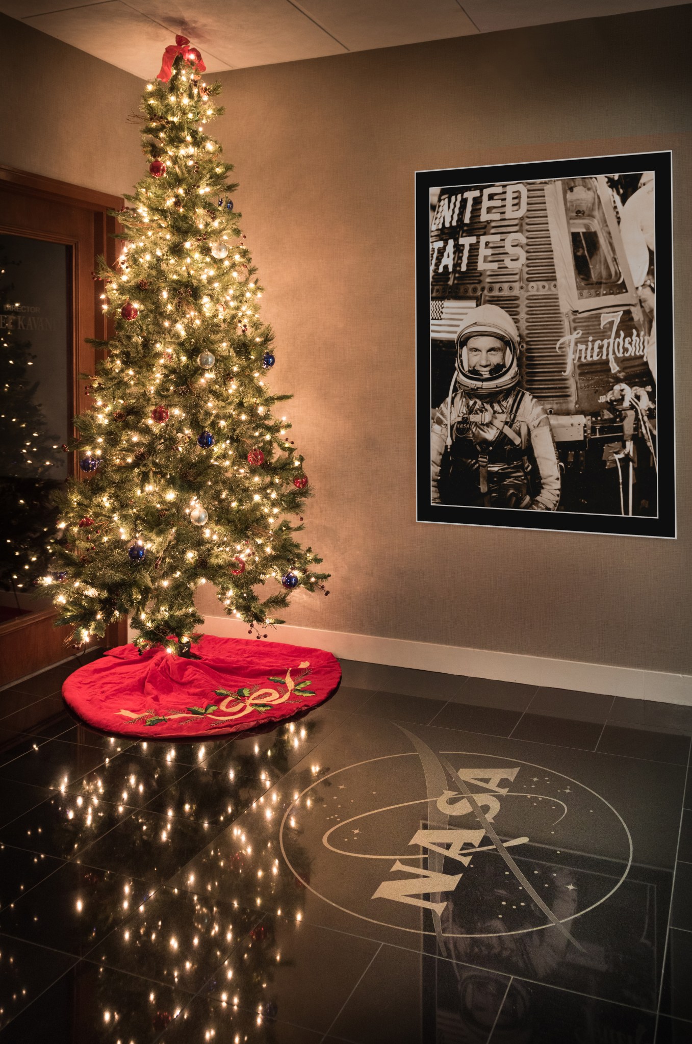 Holiday tree in the Ad building next to a photo on the wall of John Glenn and Friendship 7.