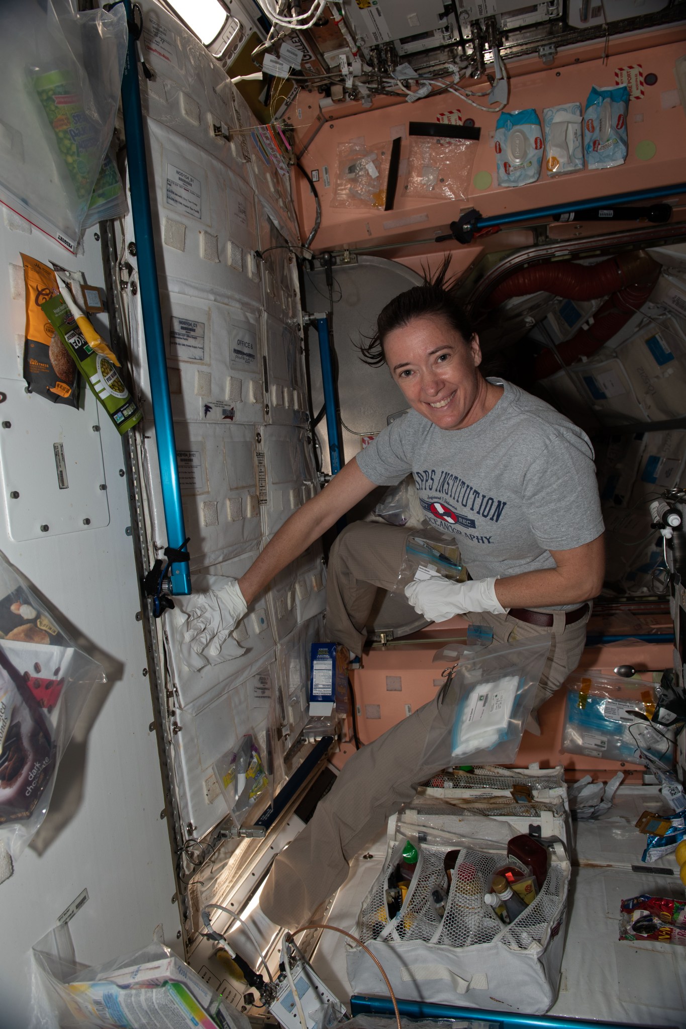 Astronaut aboard the space station wearing white gloves and using a white wipe to collect a sample from the wall
