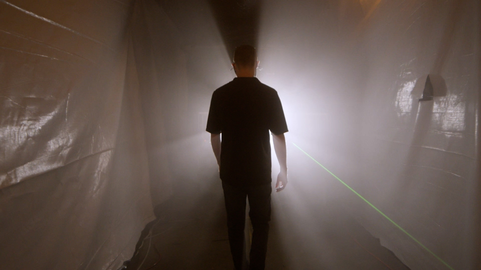 A person is silhouetted against a bright light in a space filled with fog.