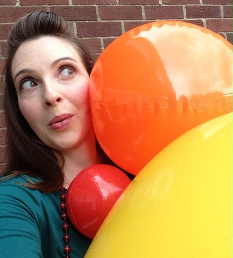 A close-up photo of a woman holding yellow, orange, and red beach balls of different sizes.
