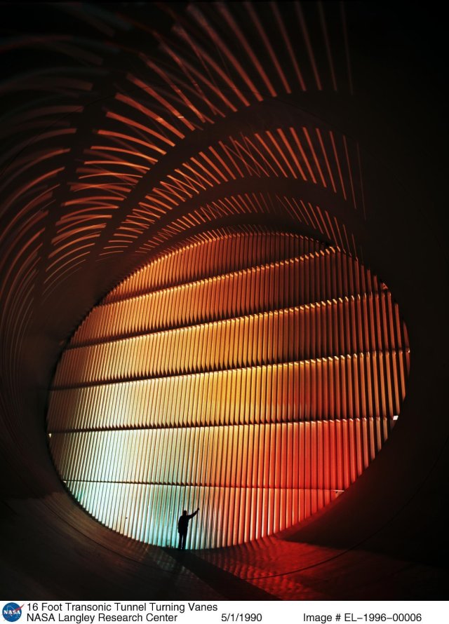 A NASA Langley employee stands in front of the 16 Foot Transonic Tunnel. The guide vanes of the tunnel, which form an ellipse 58-feet high and 82-feet wide, cut across each cylindrical tube at a 45-degree angle.