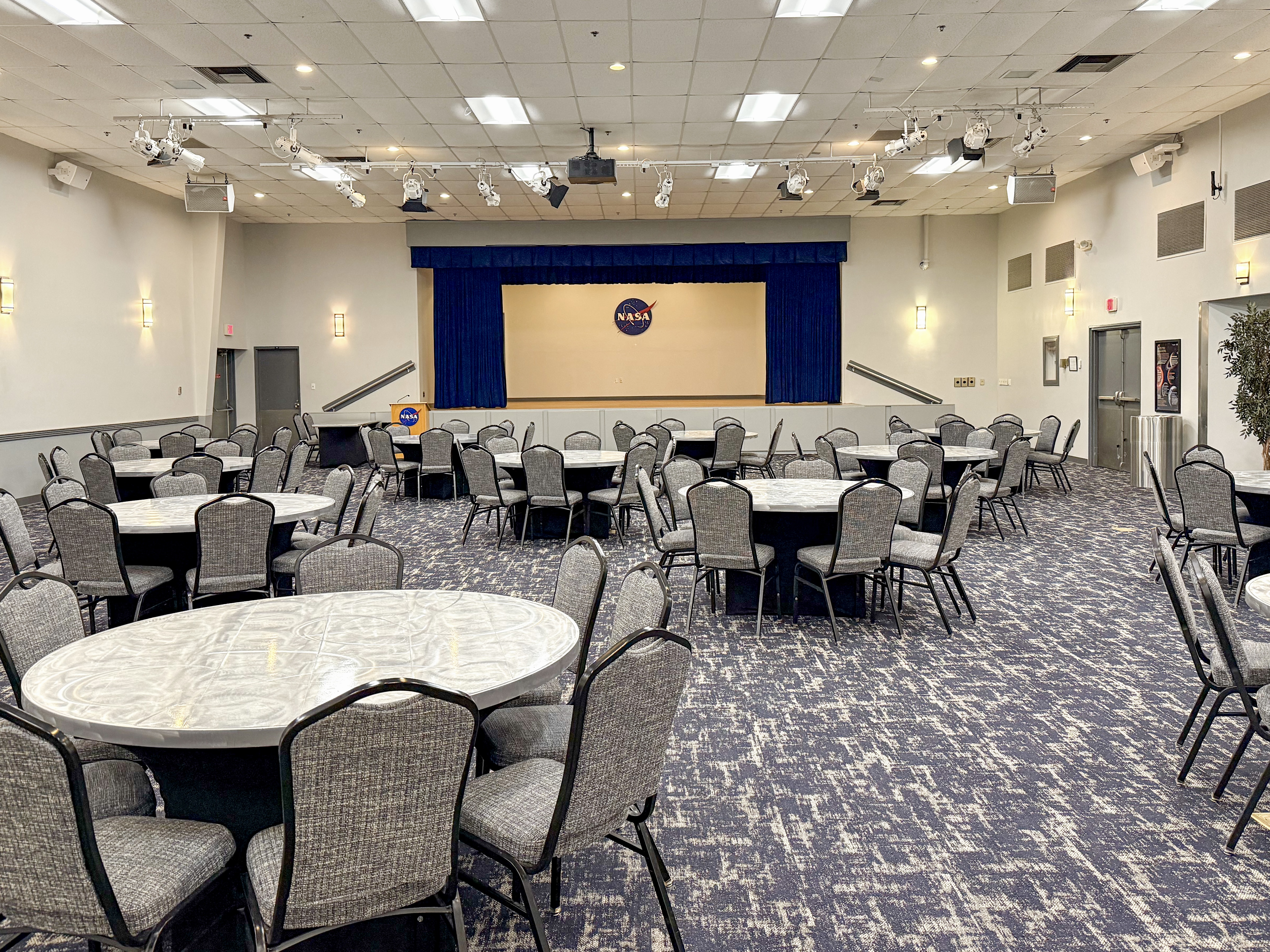 A ballroom featuring round, silver top tables and chairs.