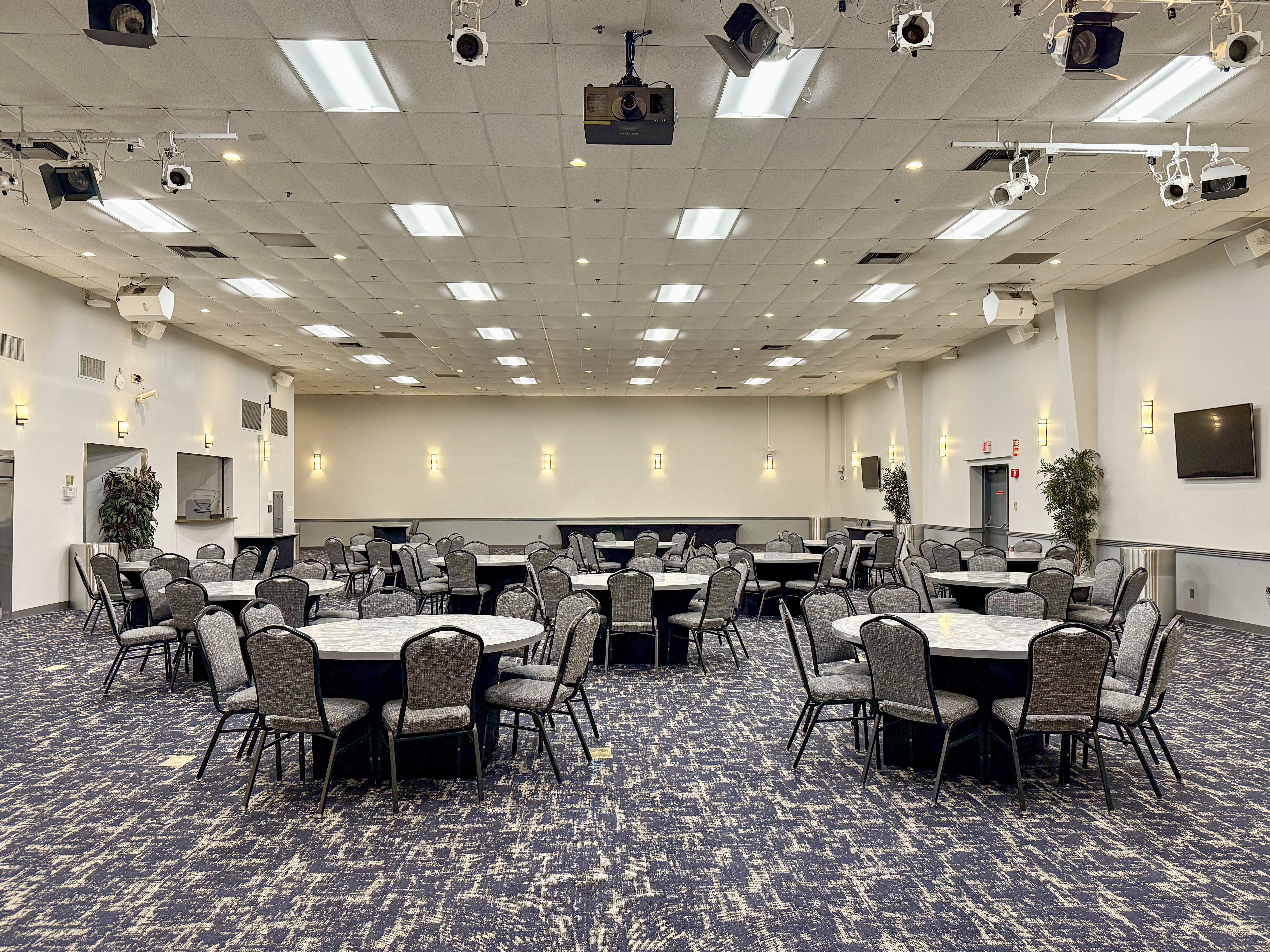 A ballroom featuring round, silver top tables and chairs.