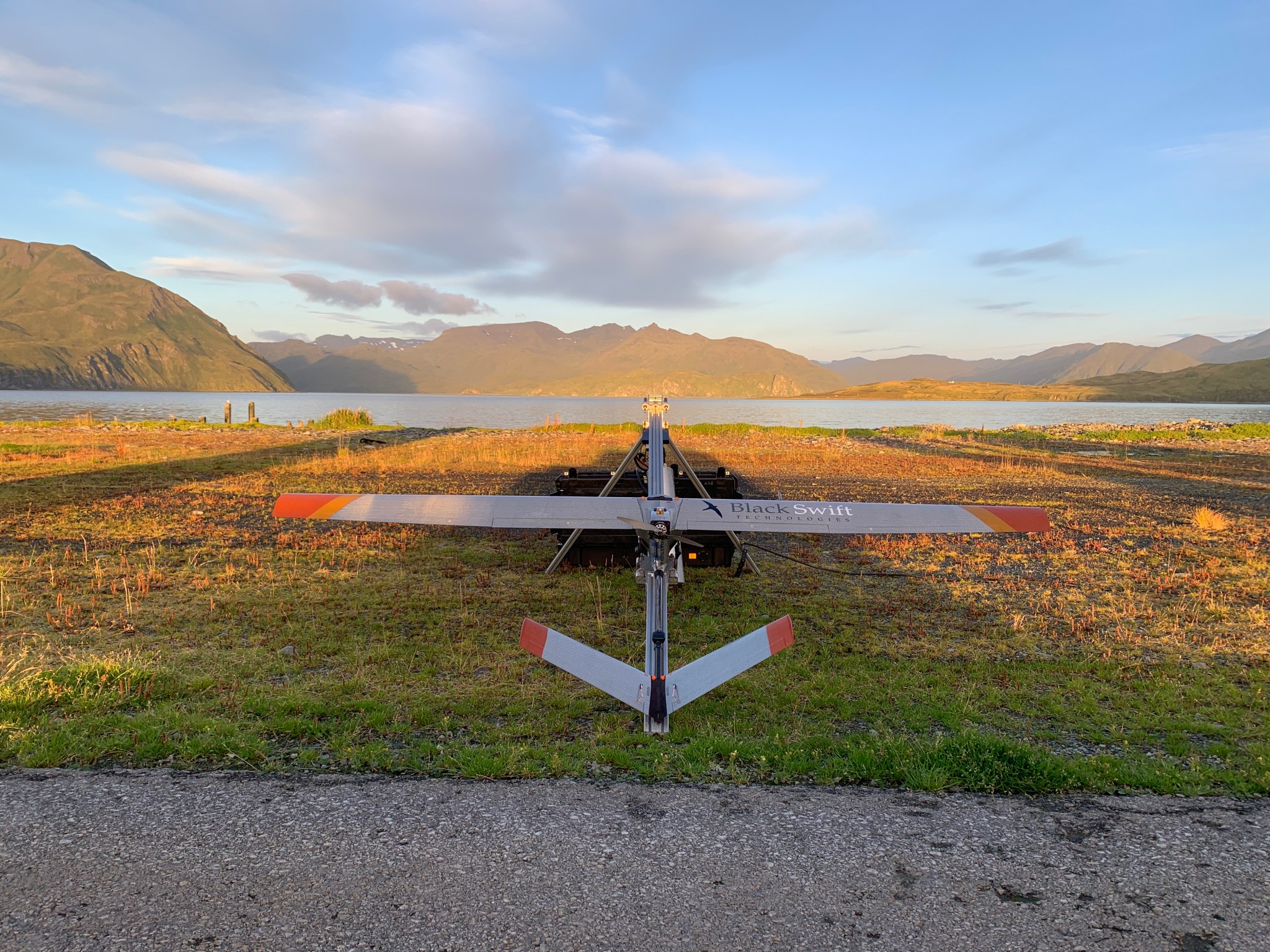 A fixed-wing unpiloted aircraft on the ground facing a lake and mountains