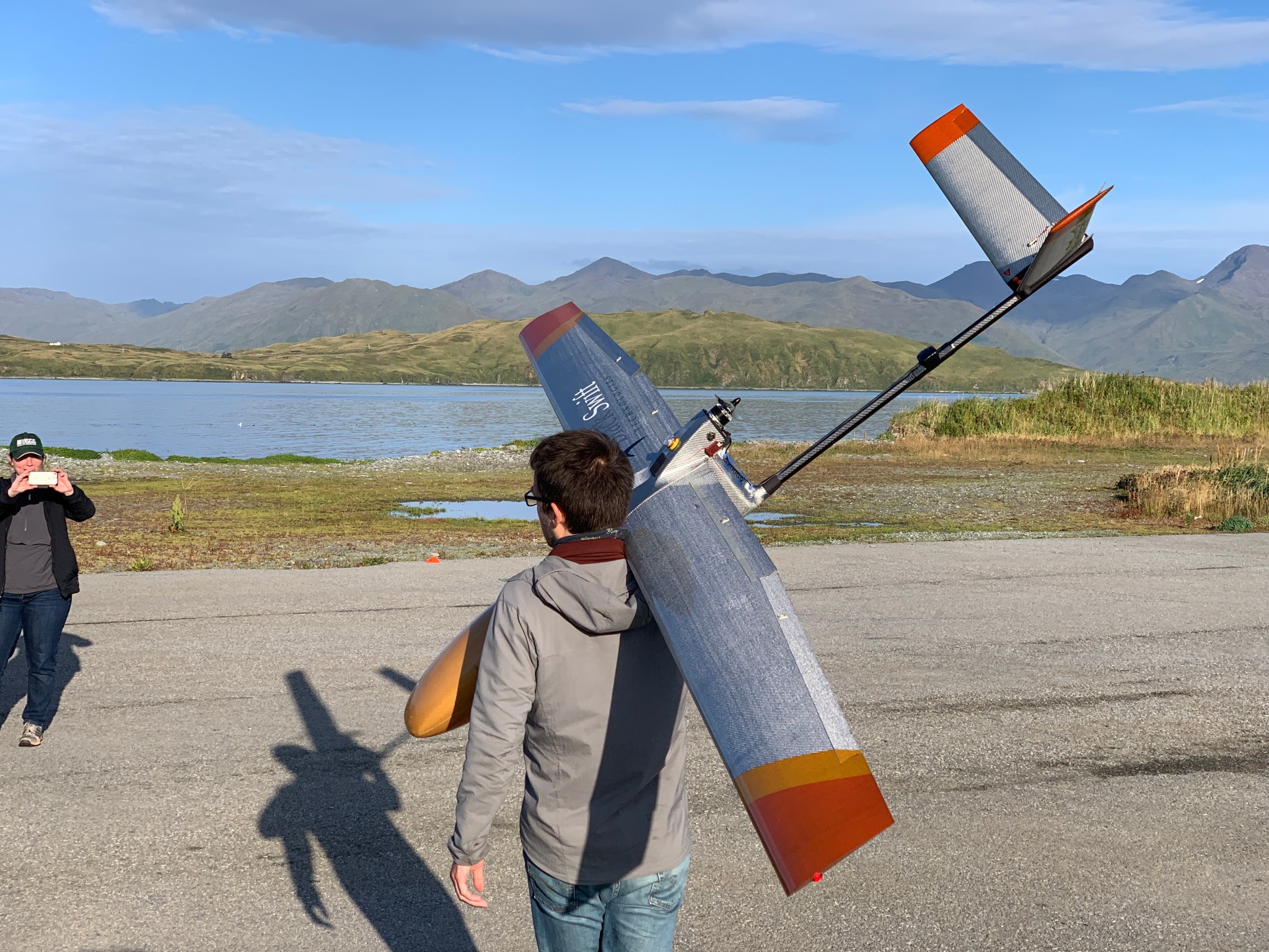 A person carrying a fixed-wing unpiloted aircraft, or drone, over his shoulder