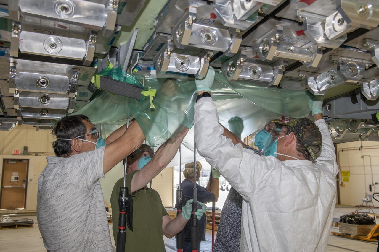 From left, Ronnie Haraguchi, Chris Mount, and Ray Sadler vacuum bag load pads on the aircraft surface of a F/A-18