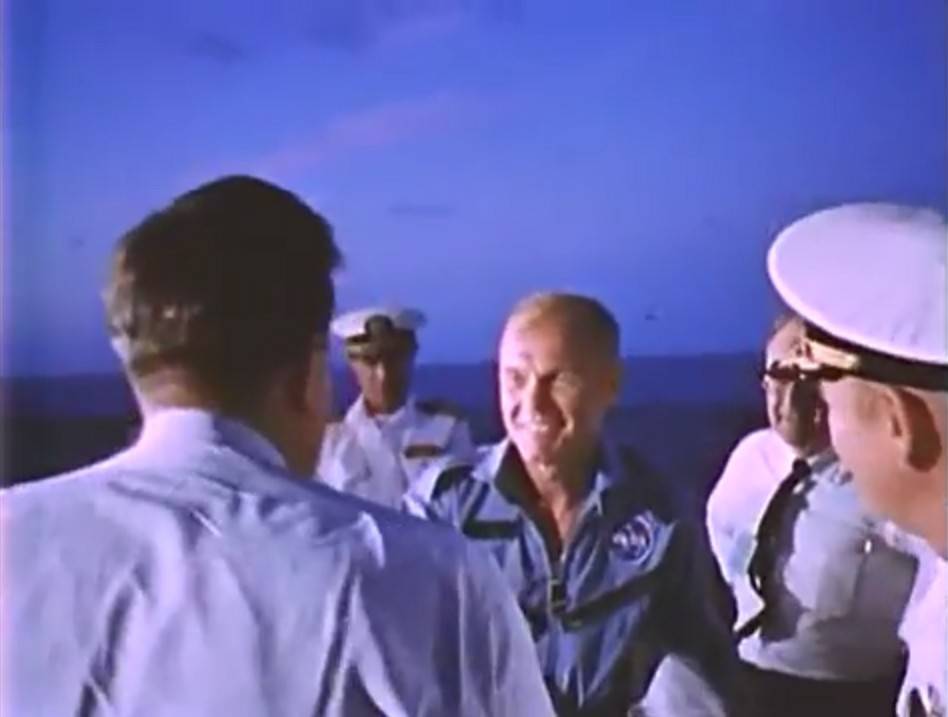 With a deep blue twilight sky behind him, John Glenn is welcomed aboard the U.S.S. Randolph after splashing down in the Atlantic Ocean.