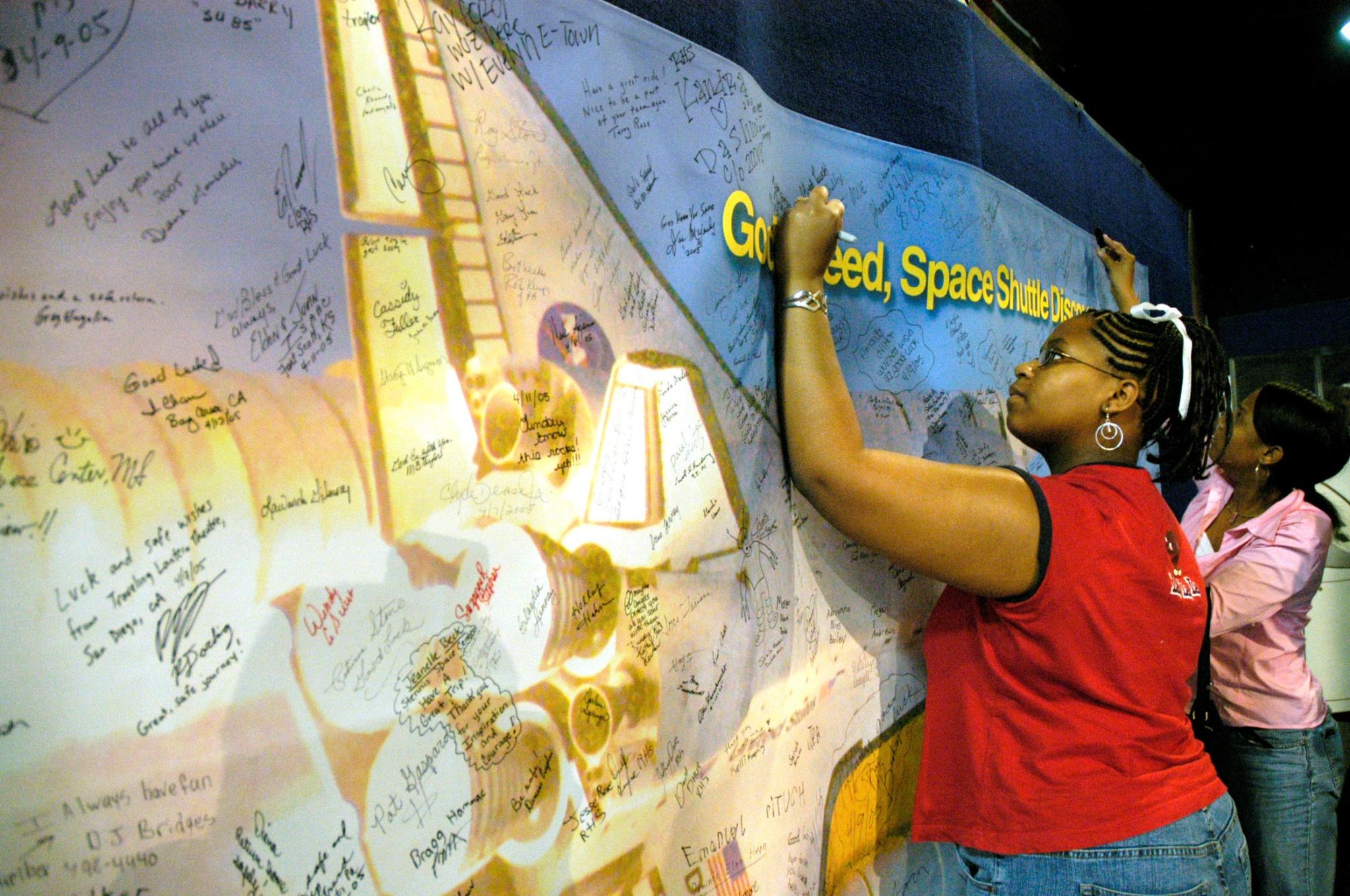 Visitors pen well wishes for the crew of the space shuttle STS-114 mission on a Return to Flight banner hanging in the former StenniSphere museum at Stennis space Center on April 22, 2005