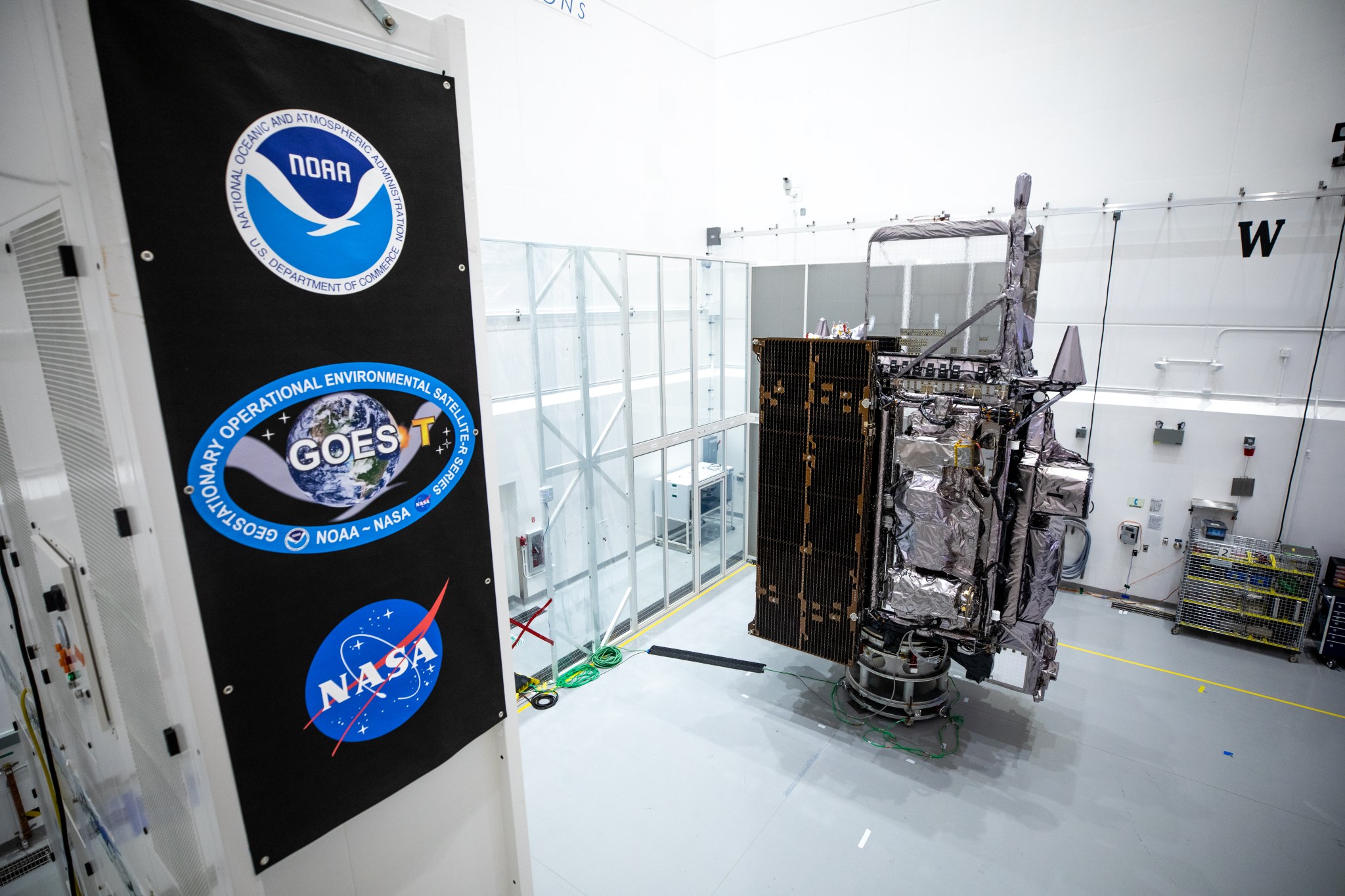 NOAA’s Geostationary Operational Environmental Satellite-T (GOES-T) is in view alongside its banner inside the Astrotech Space Operations facility in Titusville, Florida, on Jan. 20, 2022. 