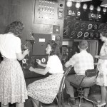 Three women and a man face computers and monitoring equipment.