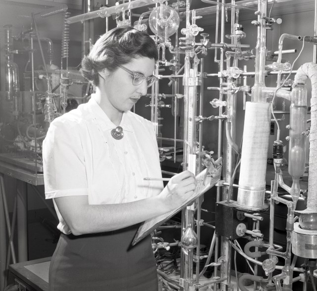 Chemist Frances Dunkel Coffin writes on a clipboard in front of lab equipment.