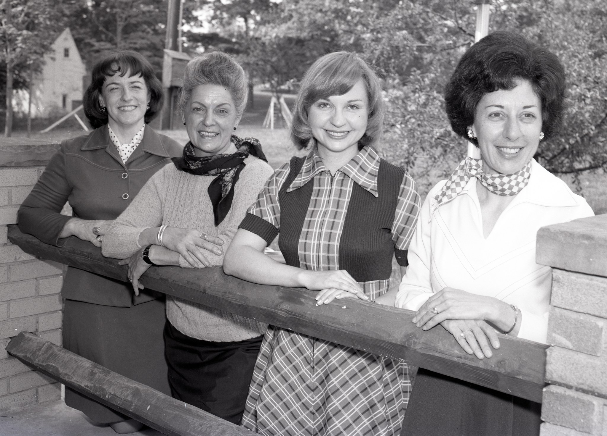Four women smile while standing at a railing.