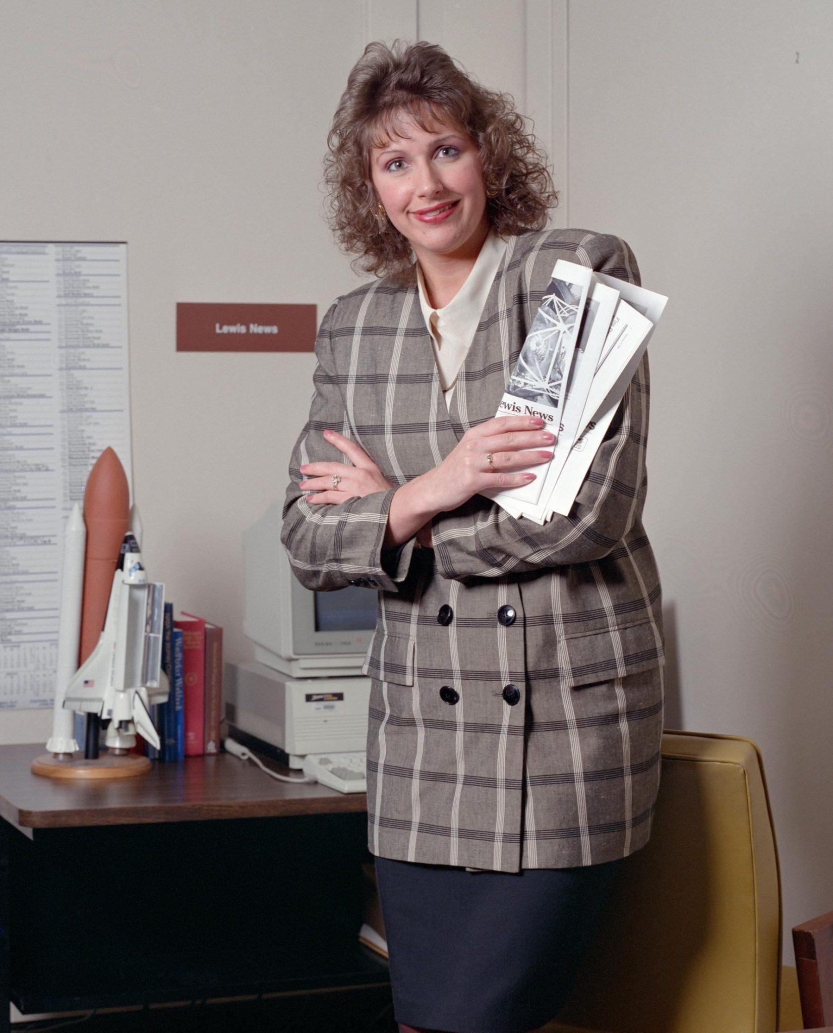 Woman standing in office holding newsletters.