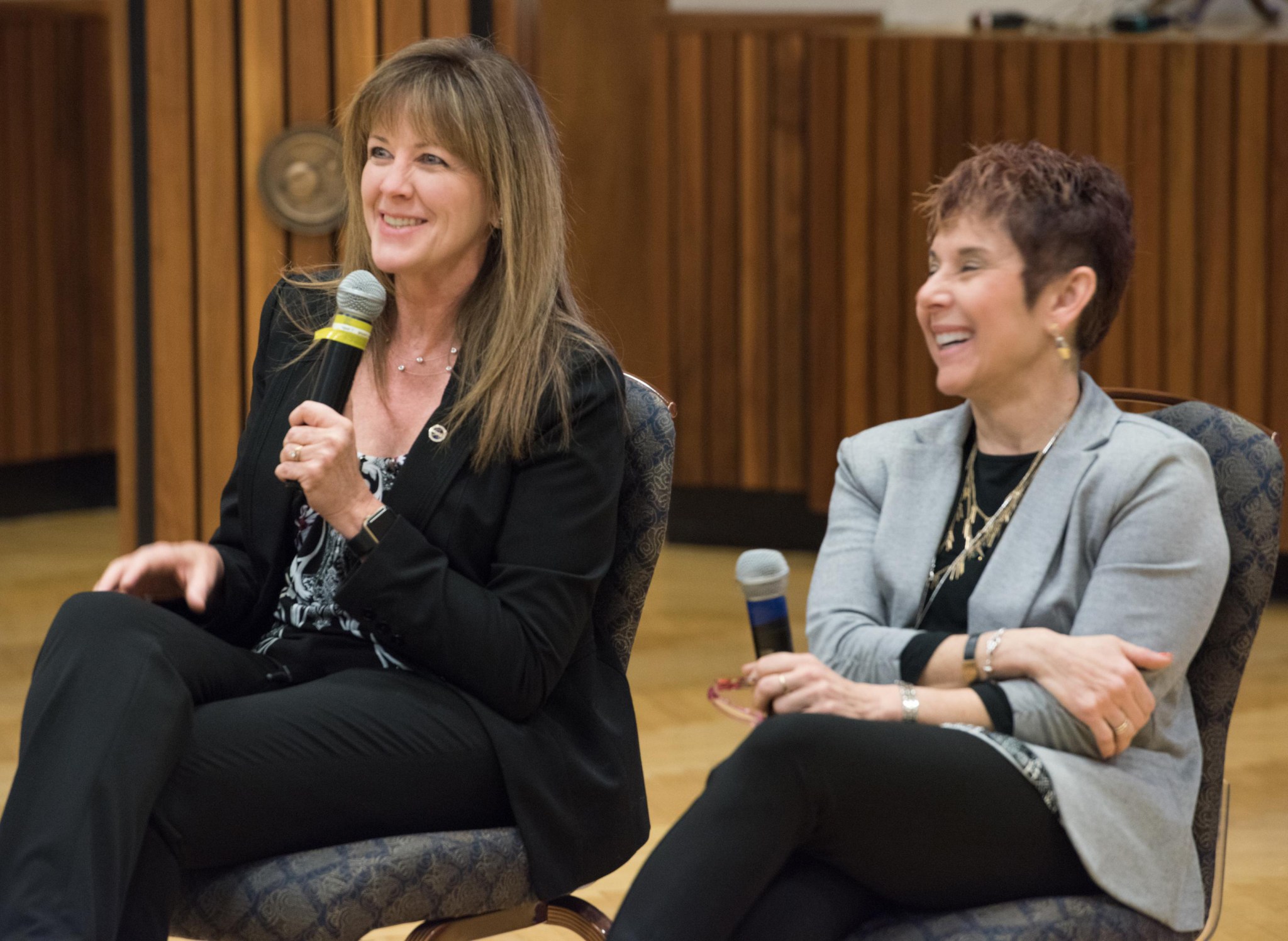 Two seated women hold microphones while answering questions.