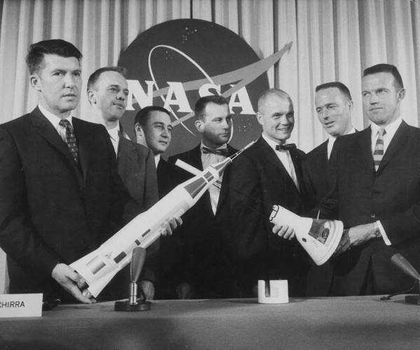 The Mercury Astronauts pose with a model rocket at a press conference