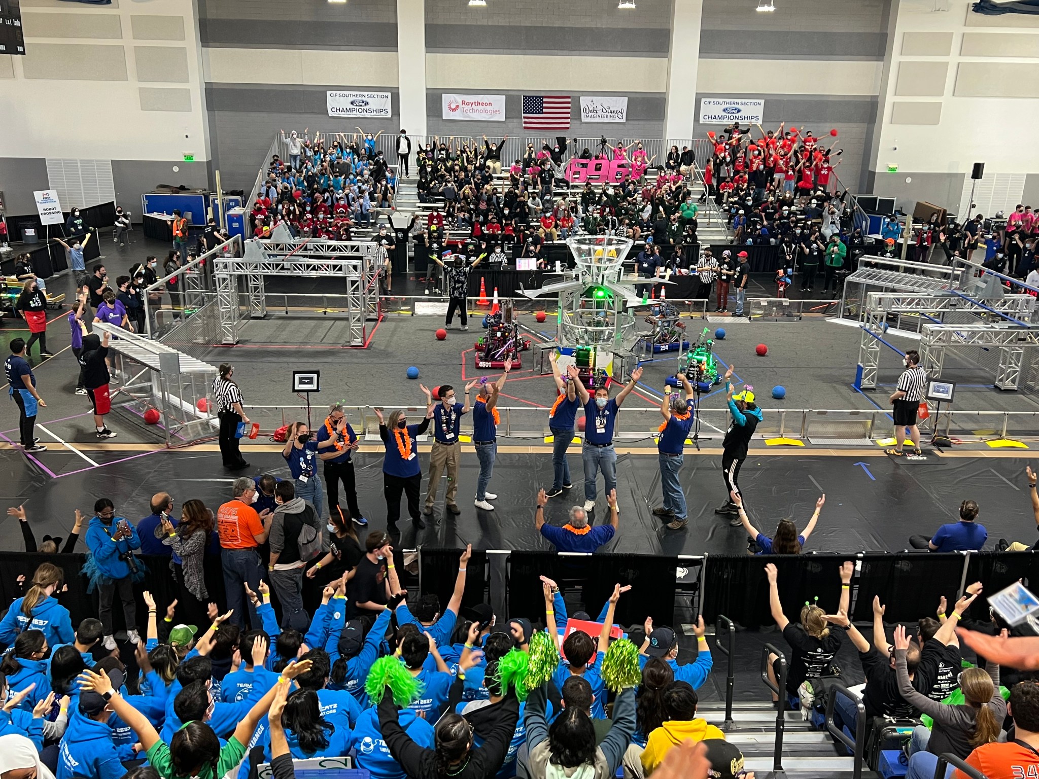 Judges, seen in navy blue at the edge of the playing field, lead students teams in a singalong of the Village People’s “YMCA” before the final playoff rounds at the 2022 Los Angeles Regional FIRST Robotics Competition.