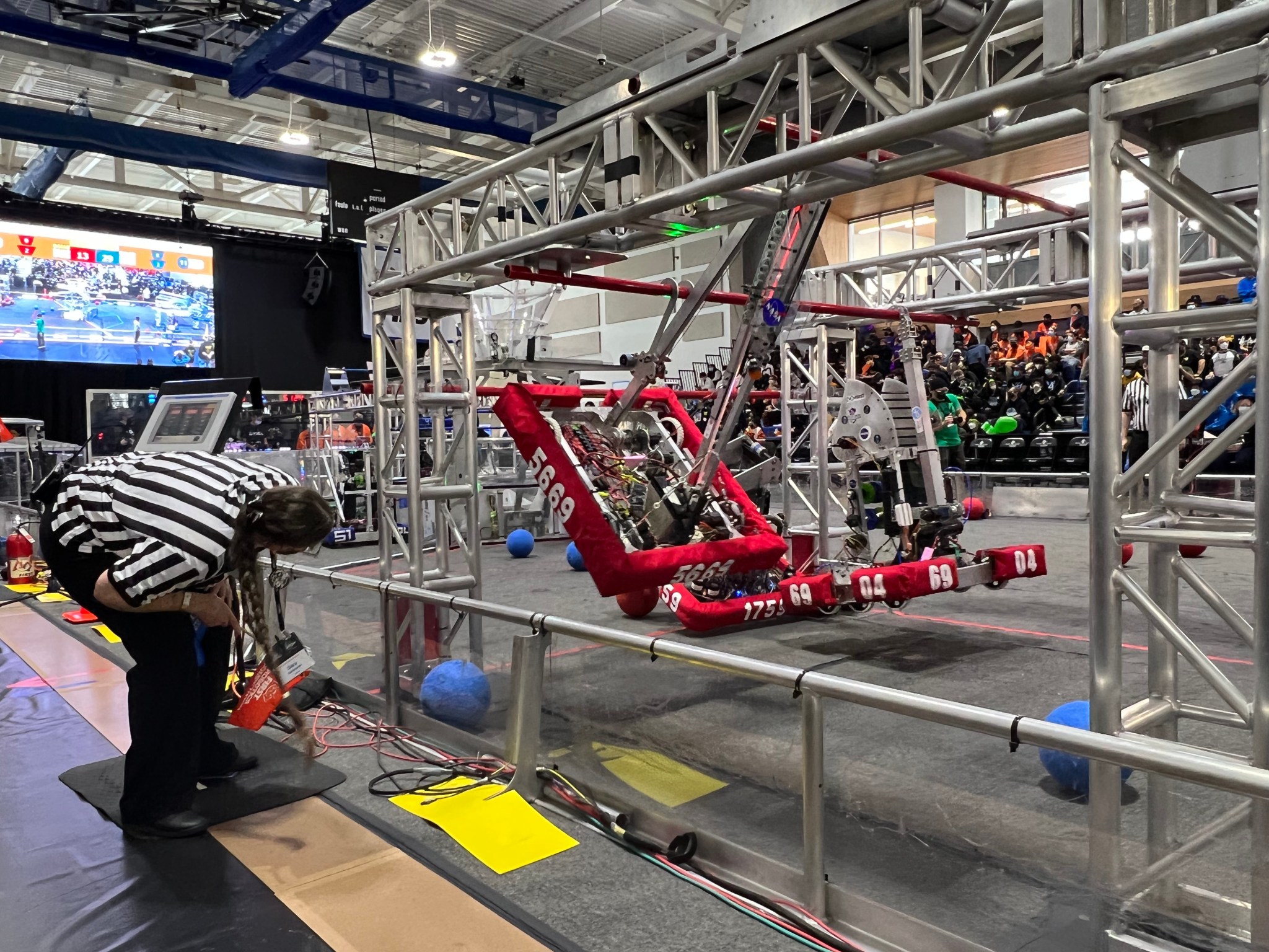 A referee at the 2022 Los Angeles Regional FIRST Robotics Competition examines robots that have managed to climb the rungs of the overhead bars in a corner of the playing field, earning them extra points.