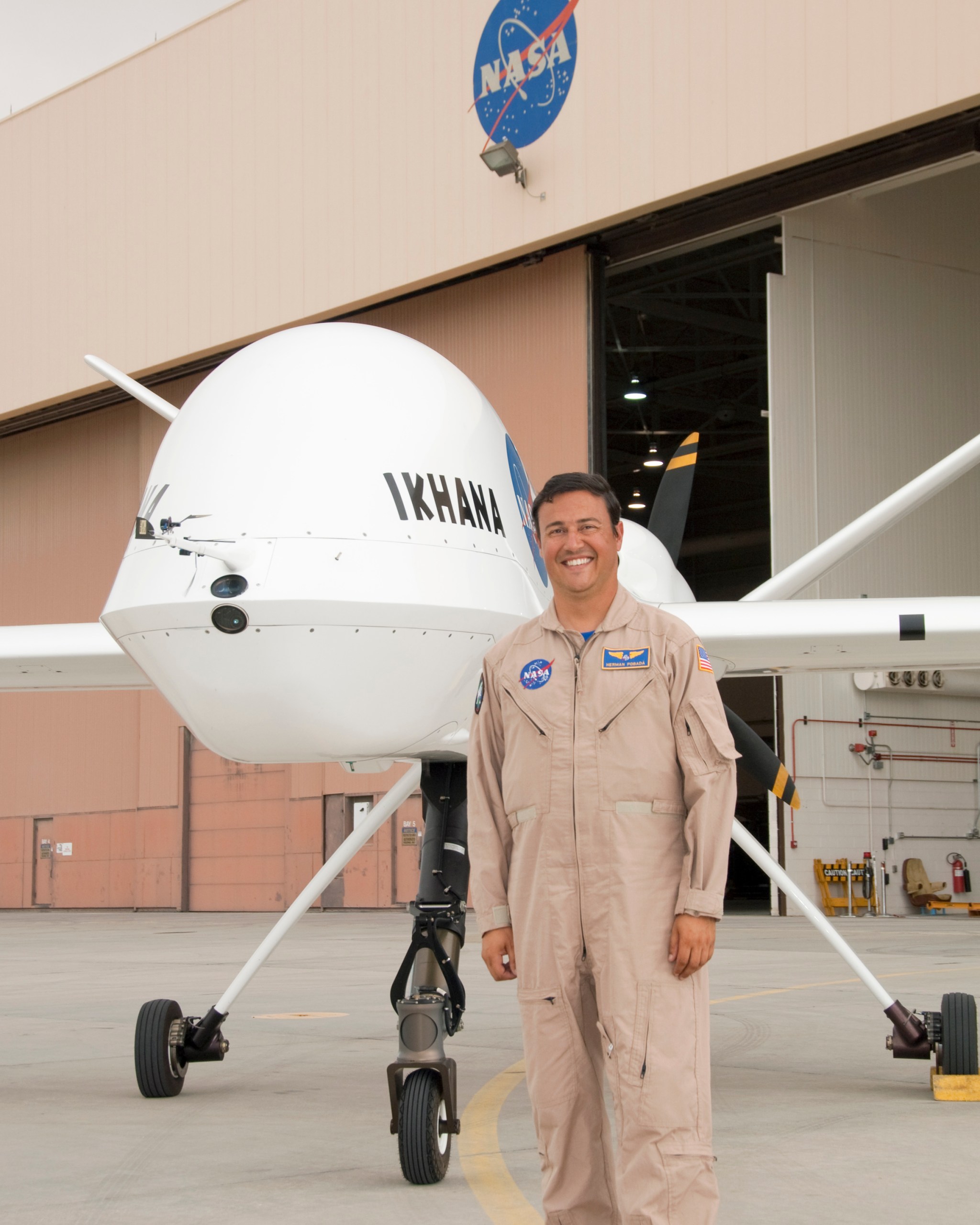 Pilot standing in front of an unmanned aircraft out side of a hangar during the day.