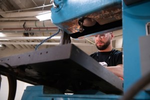 Young man in safety glasses works at a lathe.