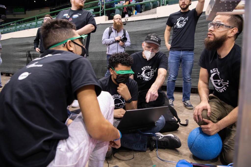 Students in masks look at computer with adult mentor talking to them.
