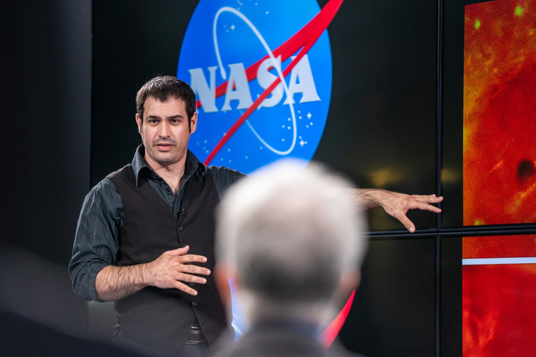Robert DePalma gestures toward a monitor; NASA logo in background