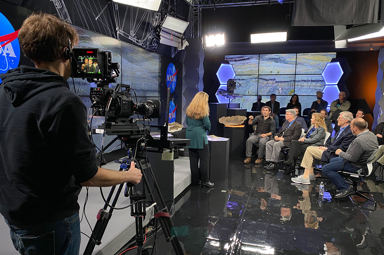 video camera operator in foreground with a seated group of scientists having a discussion